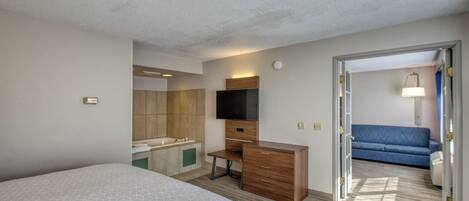 A hotel room with a bed, a desk, a television, a bathroom, and a sofa.