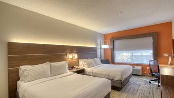 A hotel room with two beds, a desk, a chair, and a window with a view.