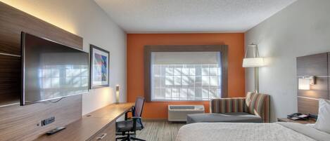Habitación de hotel con cama, escritorio, silla, televisor y ventana con persianas.