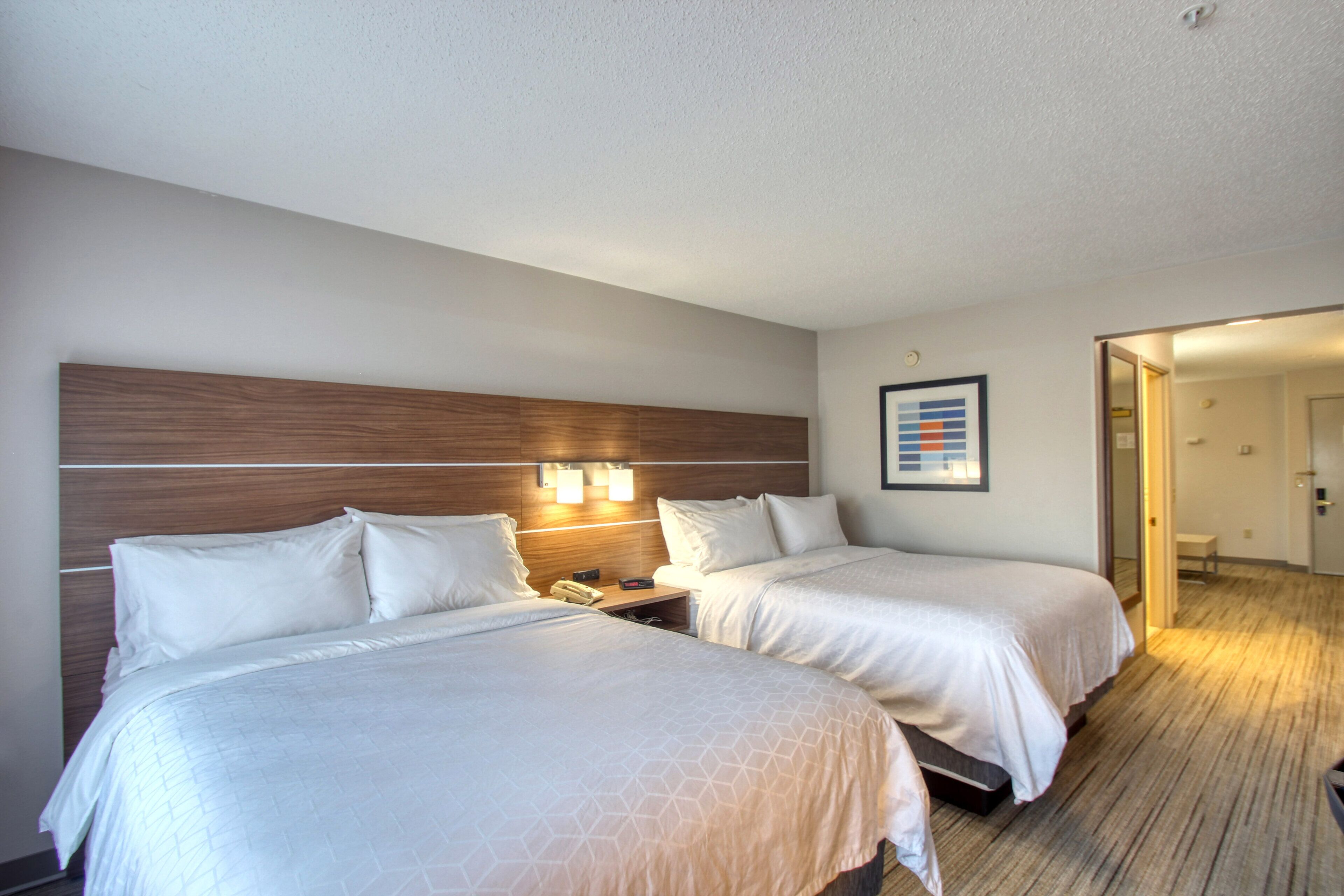 A hotel room with two beds, wooden headboard, bedside lamps, and a framed picture on the wall.