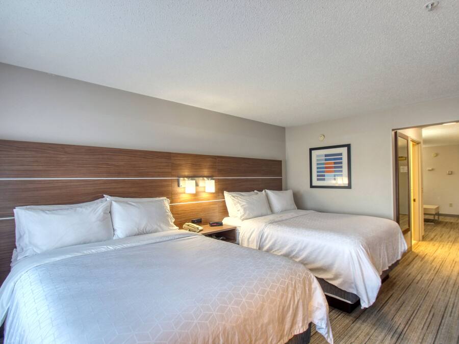 A hotel room with two beds, wooden headboard, bedside lamps, and a framed picture on the wall.