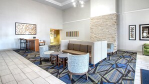 Um hall de hotel moderno com área de estar, parede de detalhes em pedra e carpete estampado.