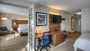 Quarto de hotel com cama, escrivaninha, cadeira, televisão e obras de arte.