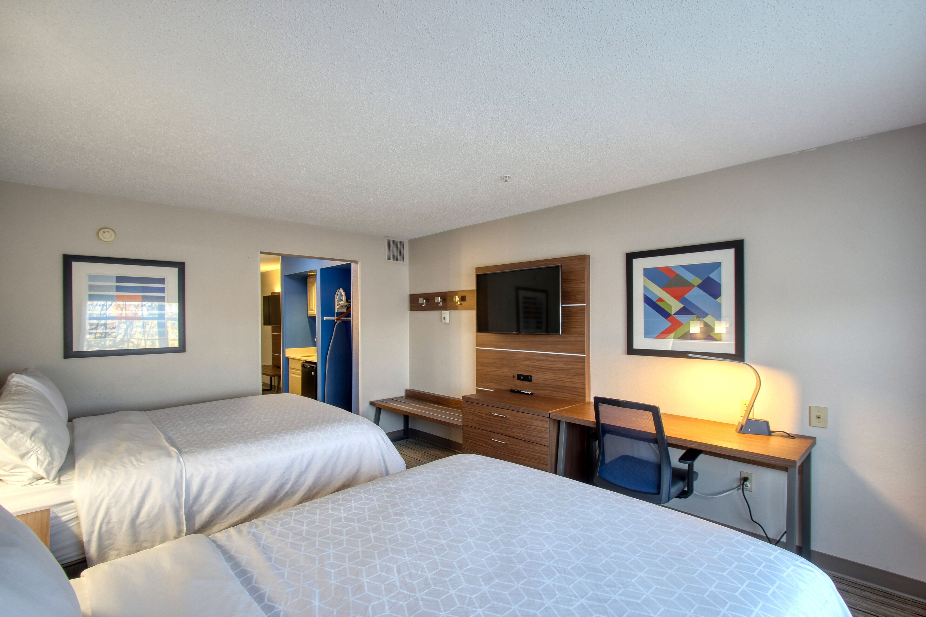 A hotel room with two beds, a desk, a TV, and artwork on the walls.