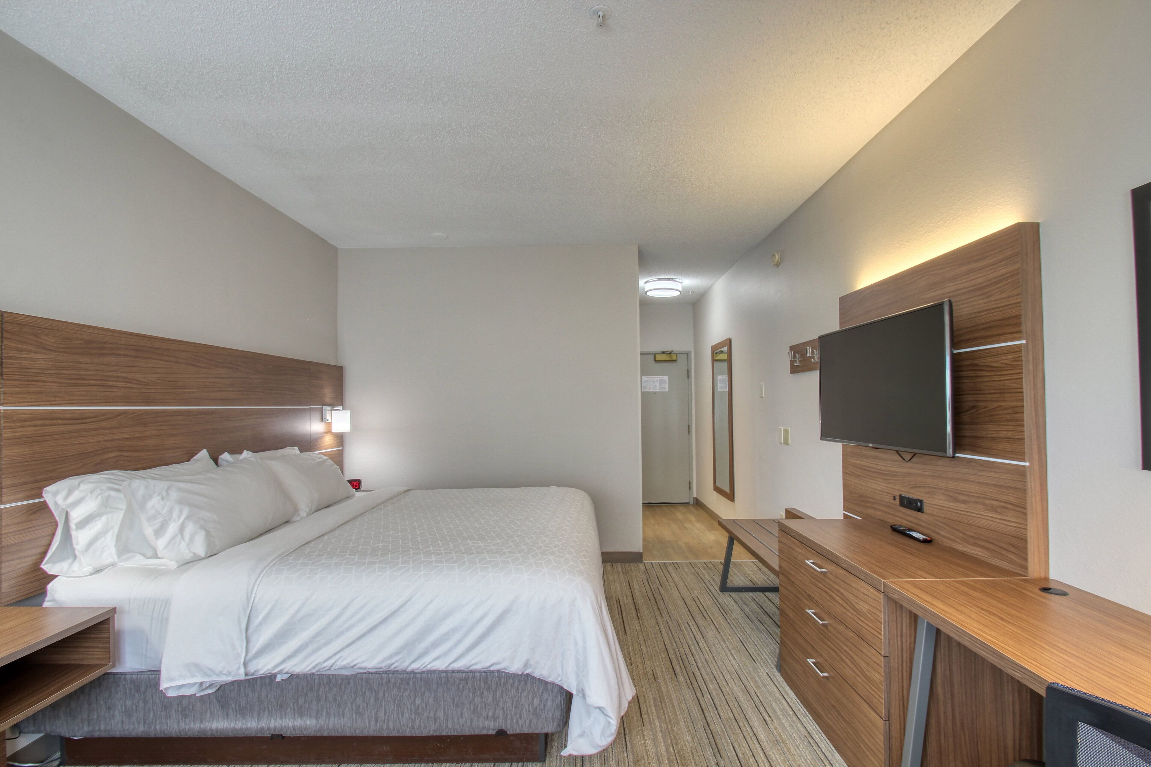 Ein modernes Hotelzimmer mit einem großen Bett, einem Holzkopfende, einem Flachbildfernseher, einem Schreibtisch und einem Spiegel.