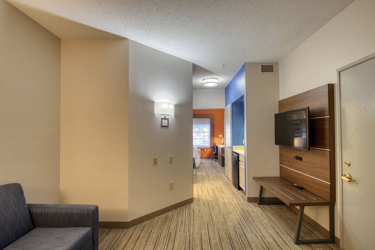 A hotel hallway with a sofa, a TV on a wooden stand, and a door.