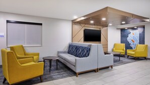A modern lobby with a grey sofa, yellow armchairs, a small table, and a large TV screen. - Holiday Inn Express Tuscola by IHG (Tuscola)