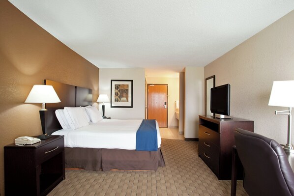 A hotel room with a bed, bedside tables, a desk with a chair, a television, and a door leading to a hallway.