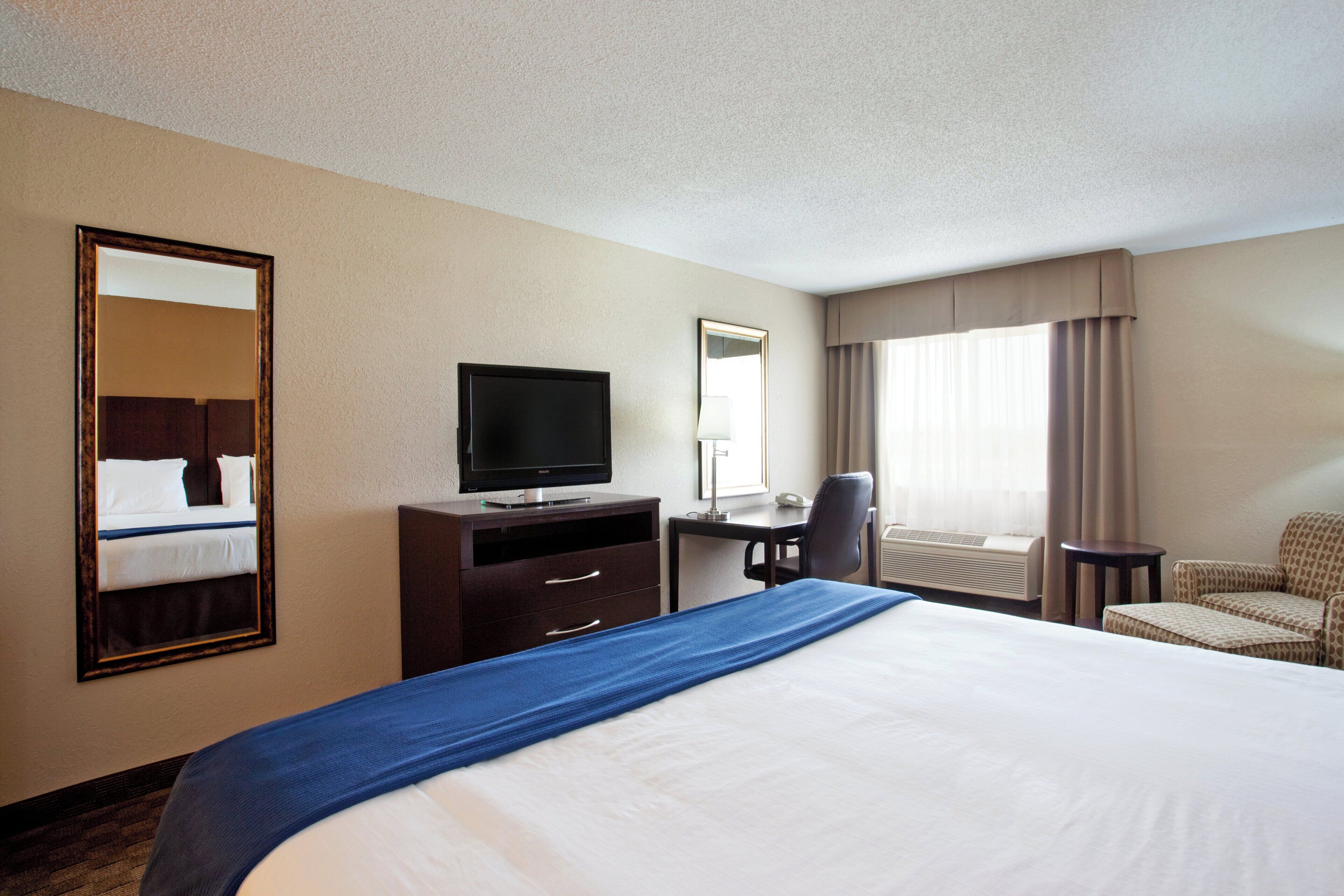 A hotel room with a bed, a desk, a television, a chair, and a window with curtains.