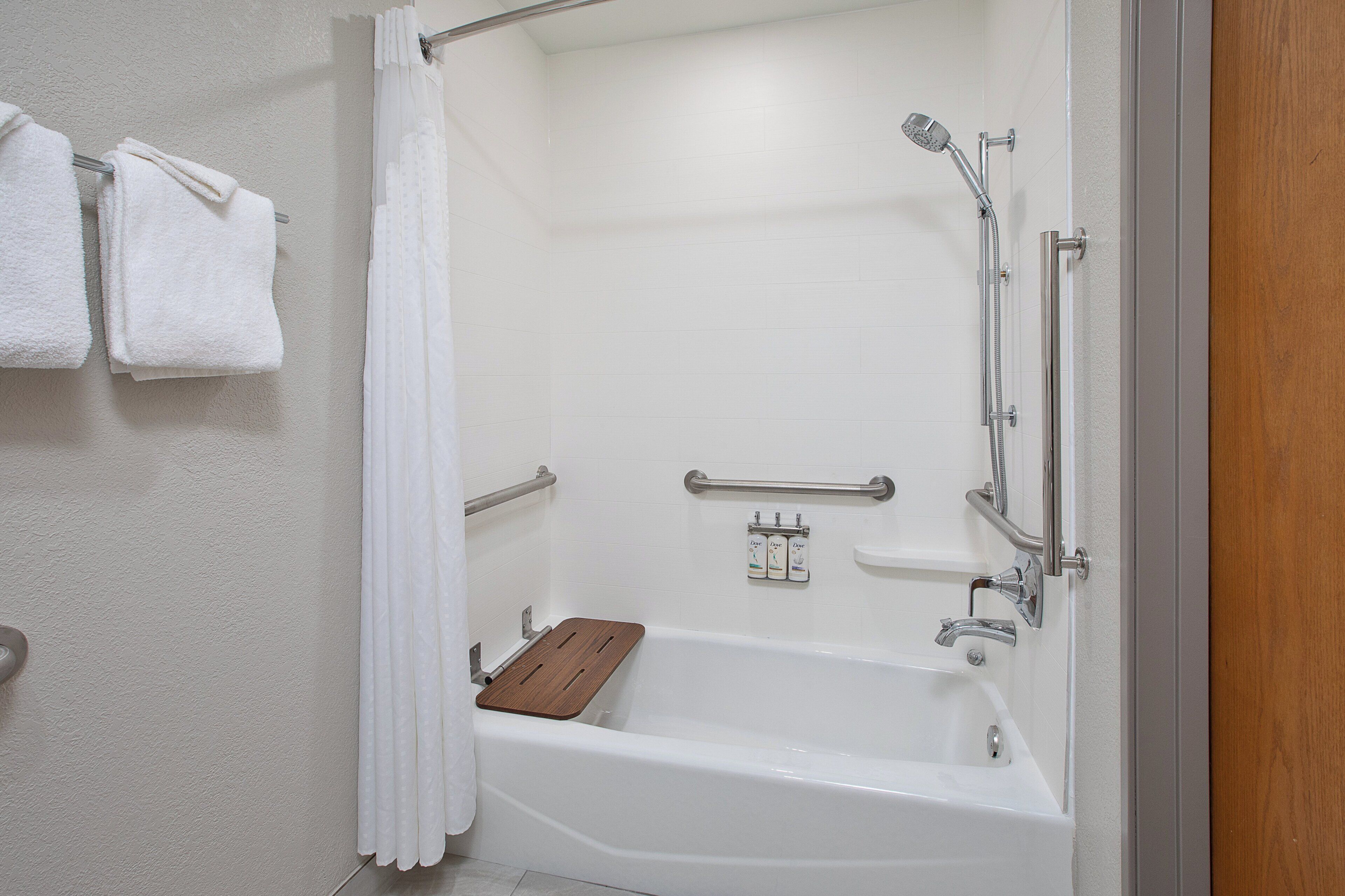 A bathroom with a bathtub, shower, and handrails.