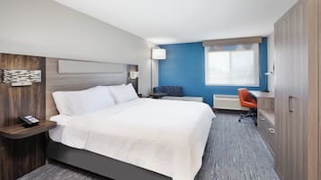 A hotel room with a bed, a desk, an orange chair, and a wardrobe.