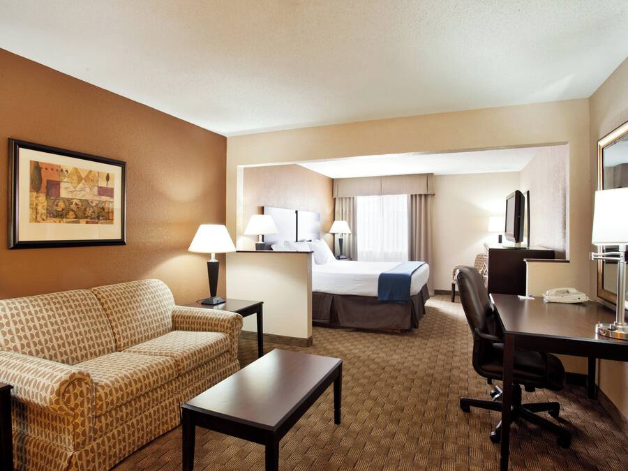 A hotel room with a sofa, a desk, a chair, a bed, and a desk lamp.