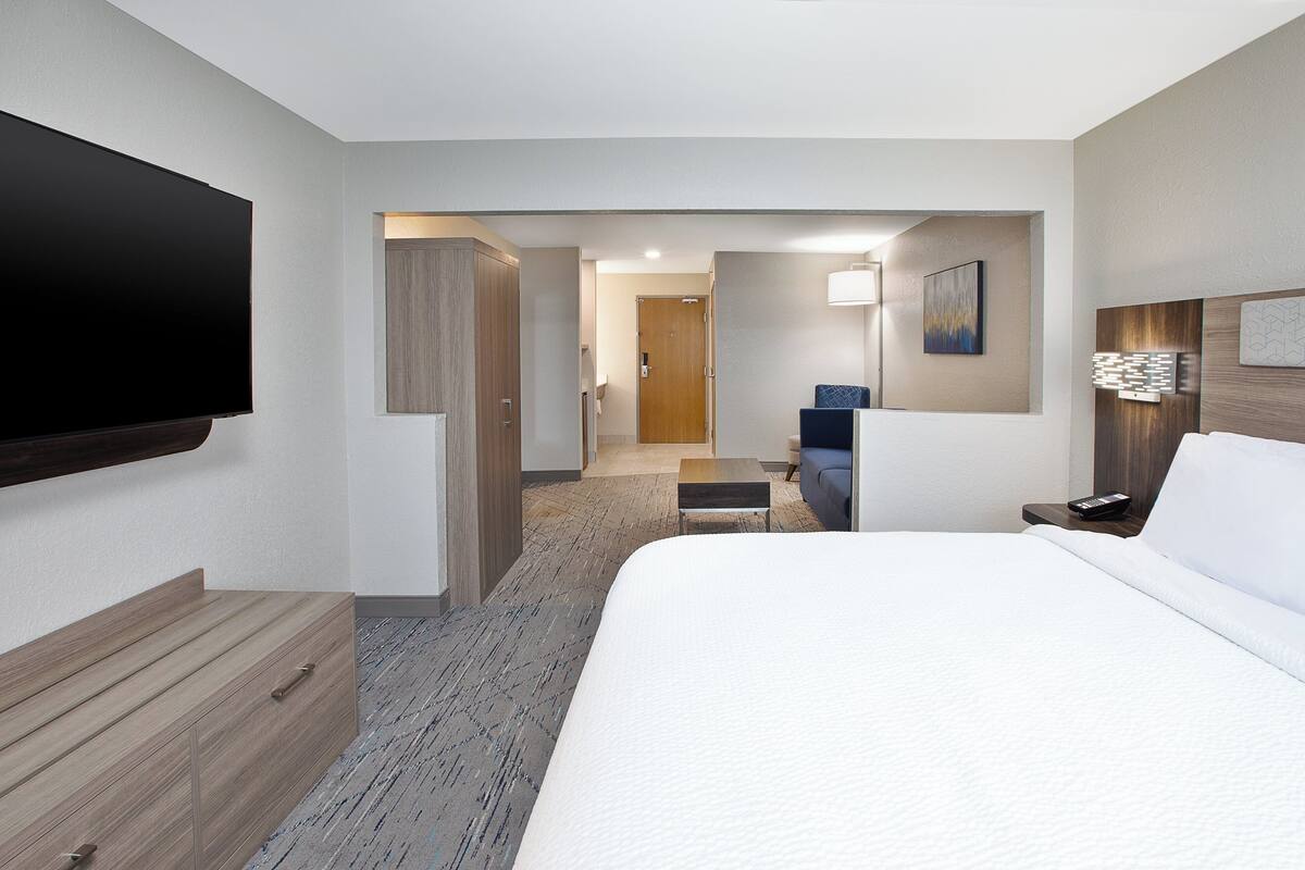 A hotel room with a large bed, a flat-screen TV, a wooden dresser, a desk, and a chair.