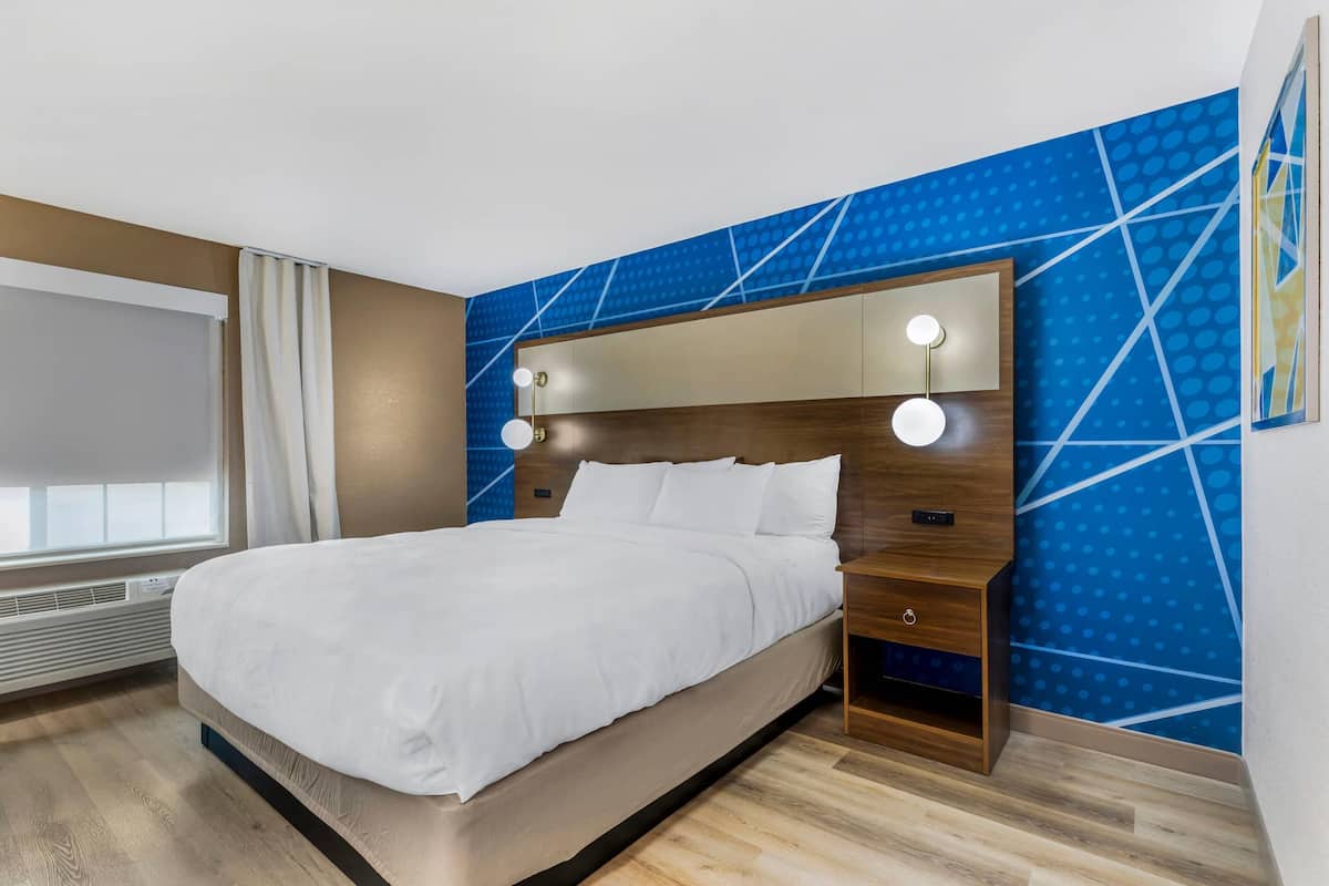 A modern hotel room with a large bed, a nightstand, and a wall-mounted light fixture.