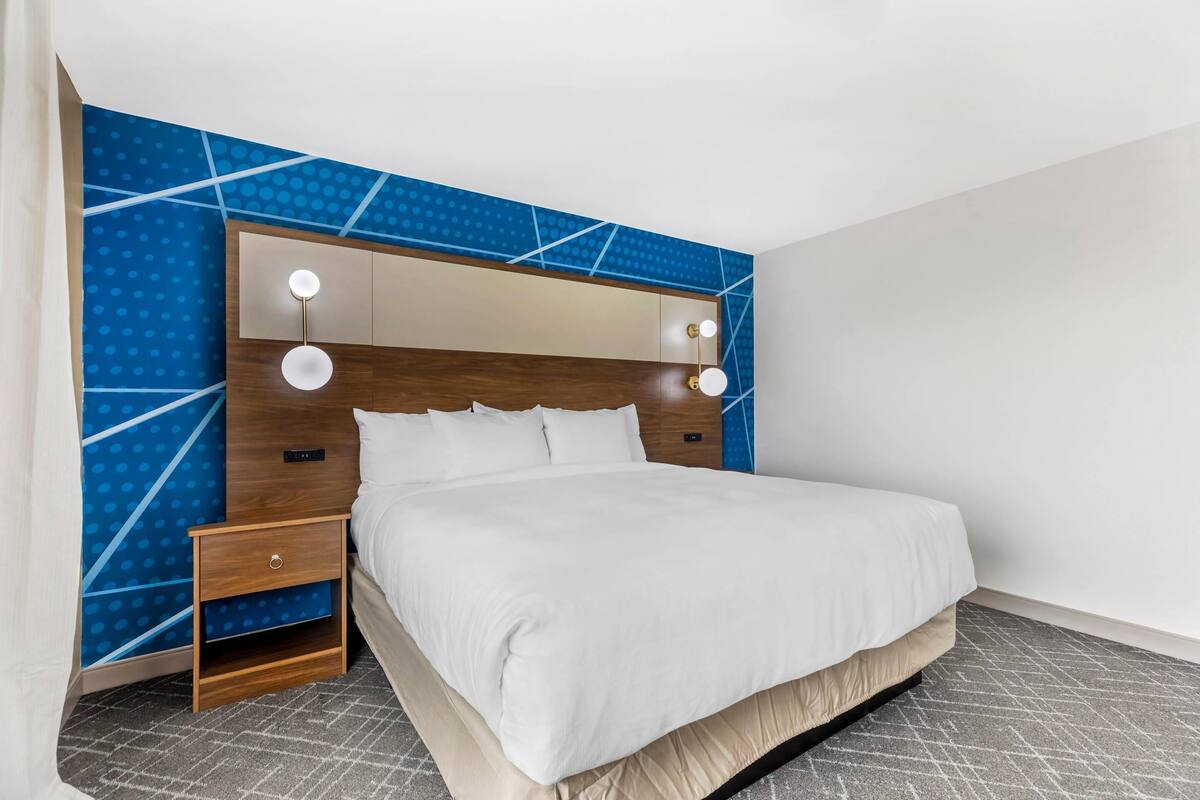 A modern hotel room with a large bed, a wooden headboard, and a blue patterned wall.