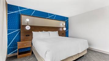 A modern hotel room with a large bed, a wooden headboard, and a blue patterned wall.