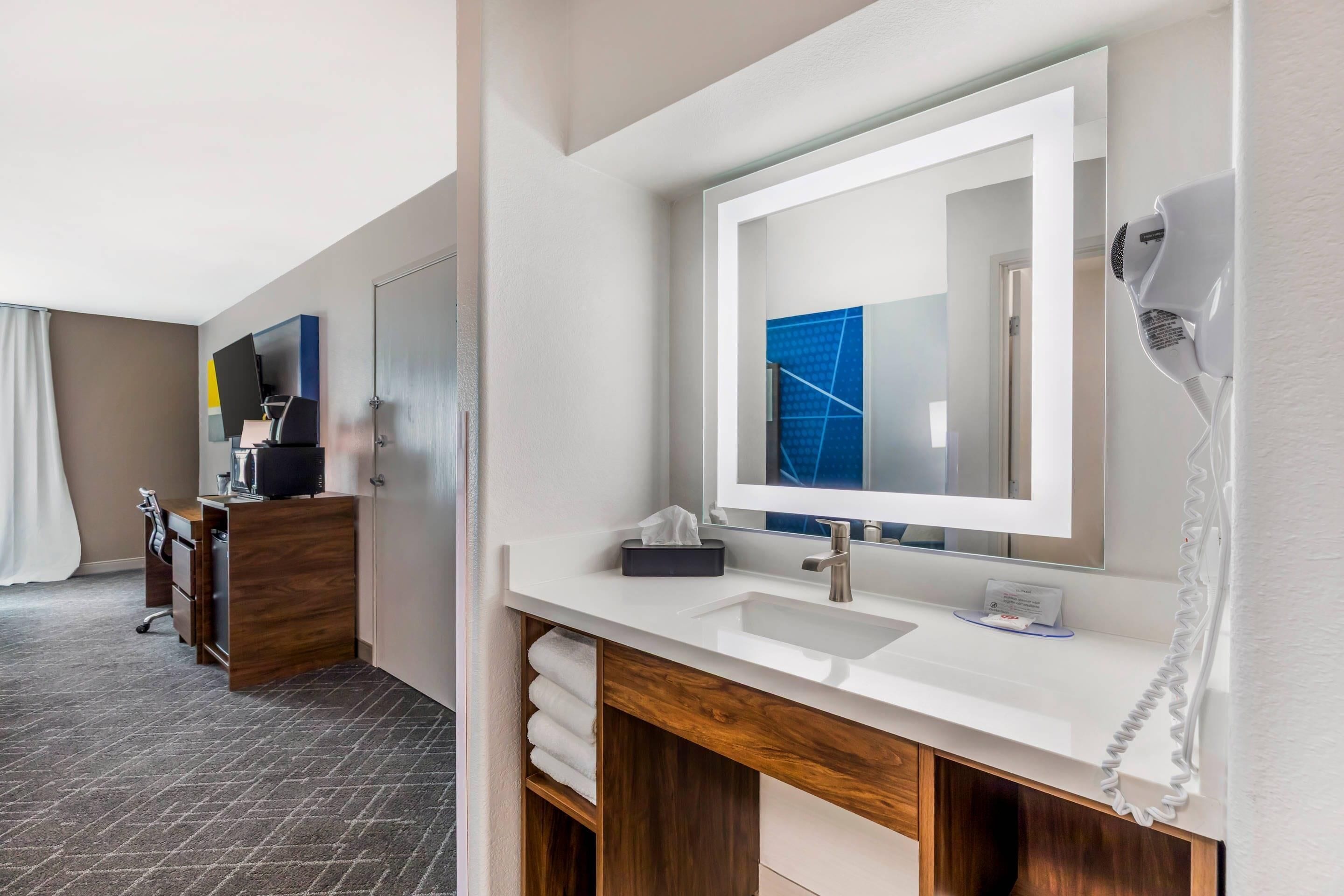 Un baño de hotel moderno con un espejo grande, un lavabo blanco y un secador de pelo en la pared.