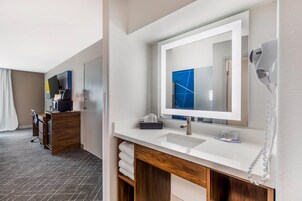 Un baño de hotel moderno con un espejo grande, un lavabo blanco y un secador de pelo en la pared.