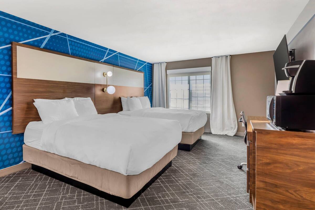 A hotel room with two beds, a TV, and a desk.
