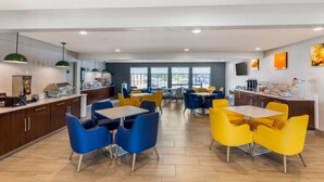 A modern dining area with blue and yellow chairs, wooden tables, and a kitchen area with a counter and appliances. - Comfort Inn & Suites Ogallala (Ogallala)