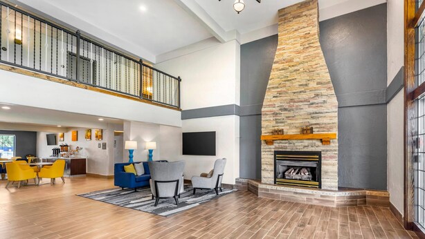 A spacious living area with a fireplace, a dining area with yellow chairs, and a kitchen in the background. - Comfort Inn & Suites Ogallala (Ogallala)