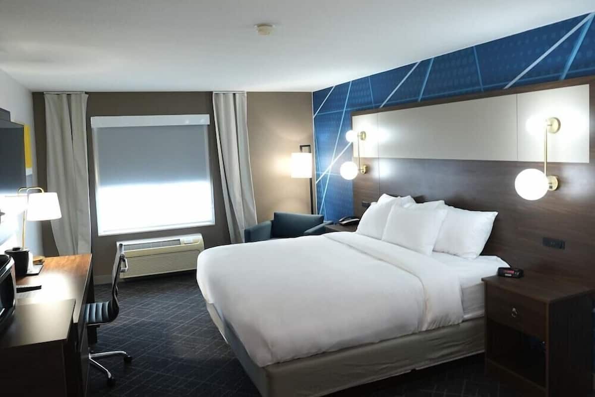 A hotel room with a bed, desk, chair, and a large window.