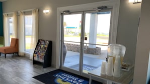 Vestíbulo de hotel con mostrador de recepción, una silla, felpudo de bienvenida y una vitrina con objetos.