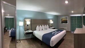 Habitación de hotel con una cama grande, dos mesitas de noche, un escritorio, una silla, un espejo, una ventana con cortinas y un televisor de pared.