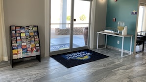 Vestíbulo de hotel con puerta de vidrio de entrada, mostrador de recepción, felpudo y exhibición de folletos de viajes.