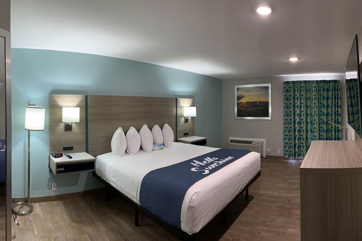 Ein Hotelzimmer mit Bett, Nachttischen, Schreibtisch, Stuhl, Lampe, einem Gemälde und einem Fenster mit Vorhängen.