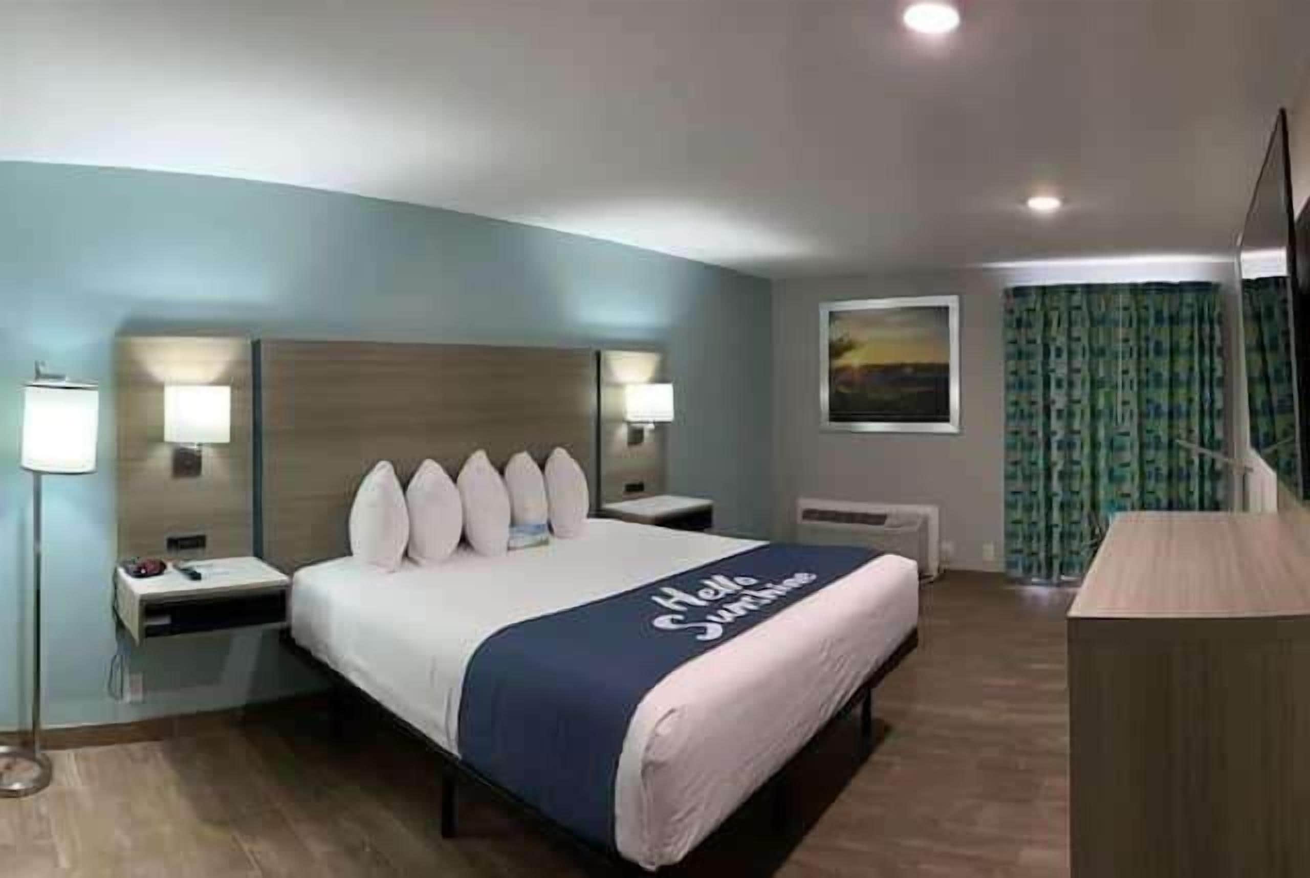 A hotel room with a bed, bedside lamps, a desk, and a view of the outdoors.