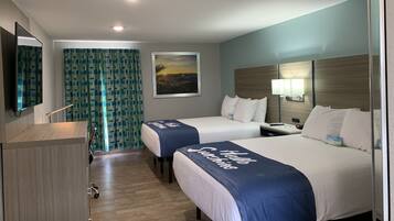 A hotel room with two beds, a desk, a mirror, a painting, and a curtain.