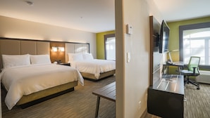 A hotel room with two beds, a desk, a chair, a TV, and a window.