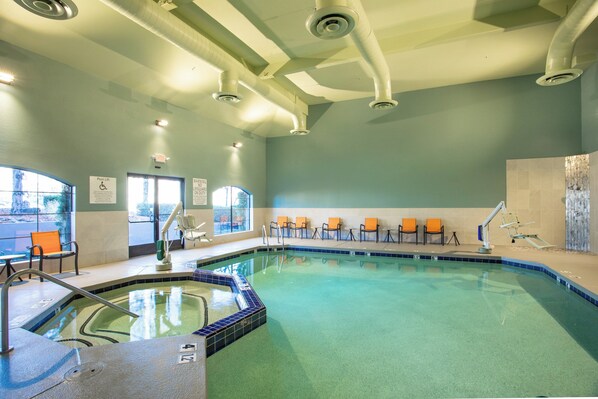 An indoor swimming pool with a clear water area, a diving board, and several lounge chairs.