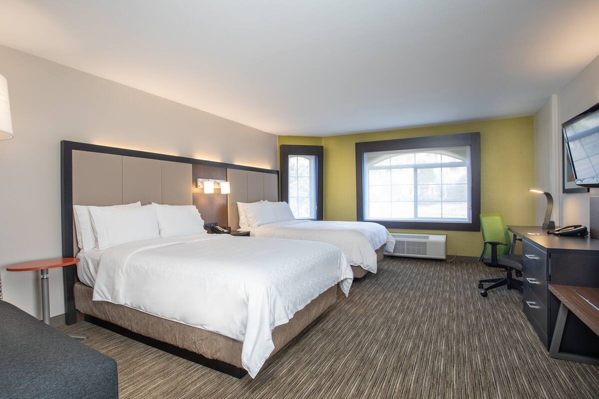 A hotel room with two beds, a desk, a chair, a TV, and a window.