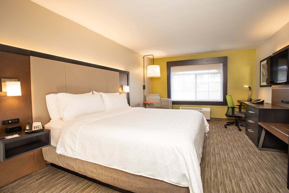 A hotel room with a large bed, bedside table with a phone and lamp, a desk with a chair, and a TV on a stand.