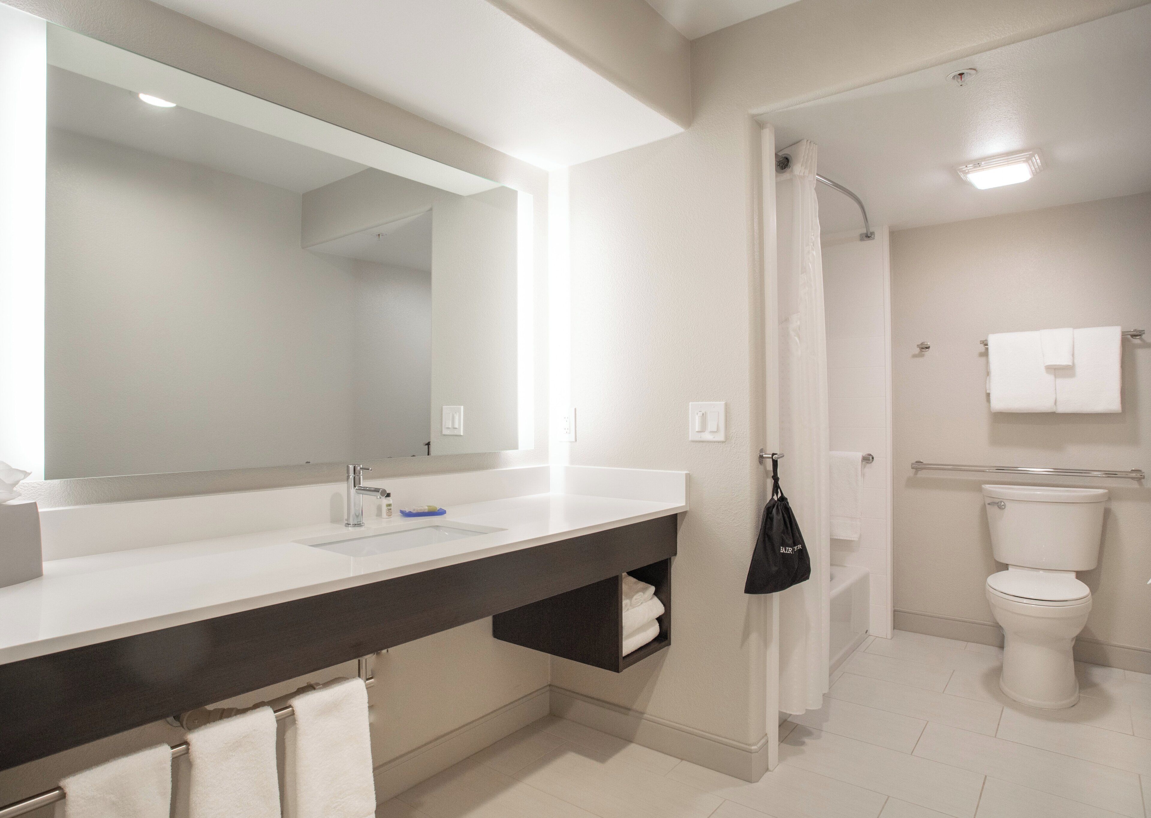 A modern bathroom with a large mirror, a sink, a toilet, and a shower area.
