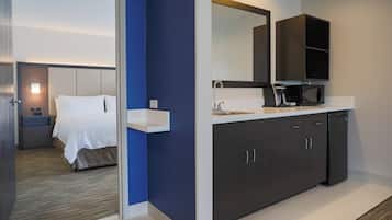 Quarto de hotel moderno com cama, banheiro com pia, espelho e micro-ondas.