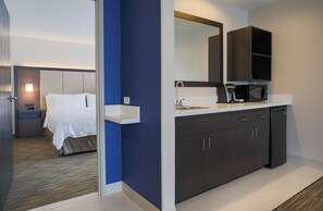 A modern hotel room with a bed, a bathroom with a sink, mirror, and a microwave.