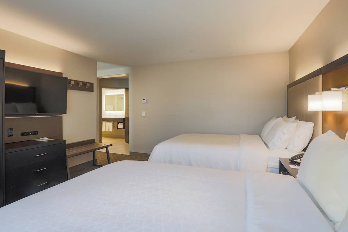 A hotel room with two beds, a desk, a TV, and a bathroom visible through an open door.