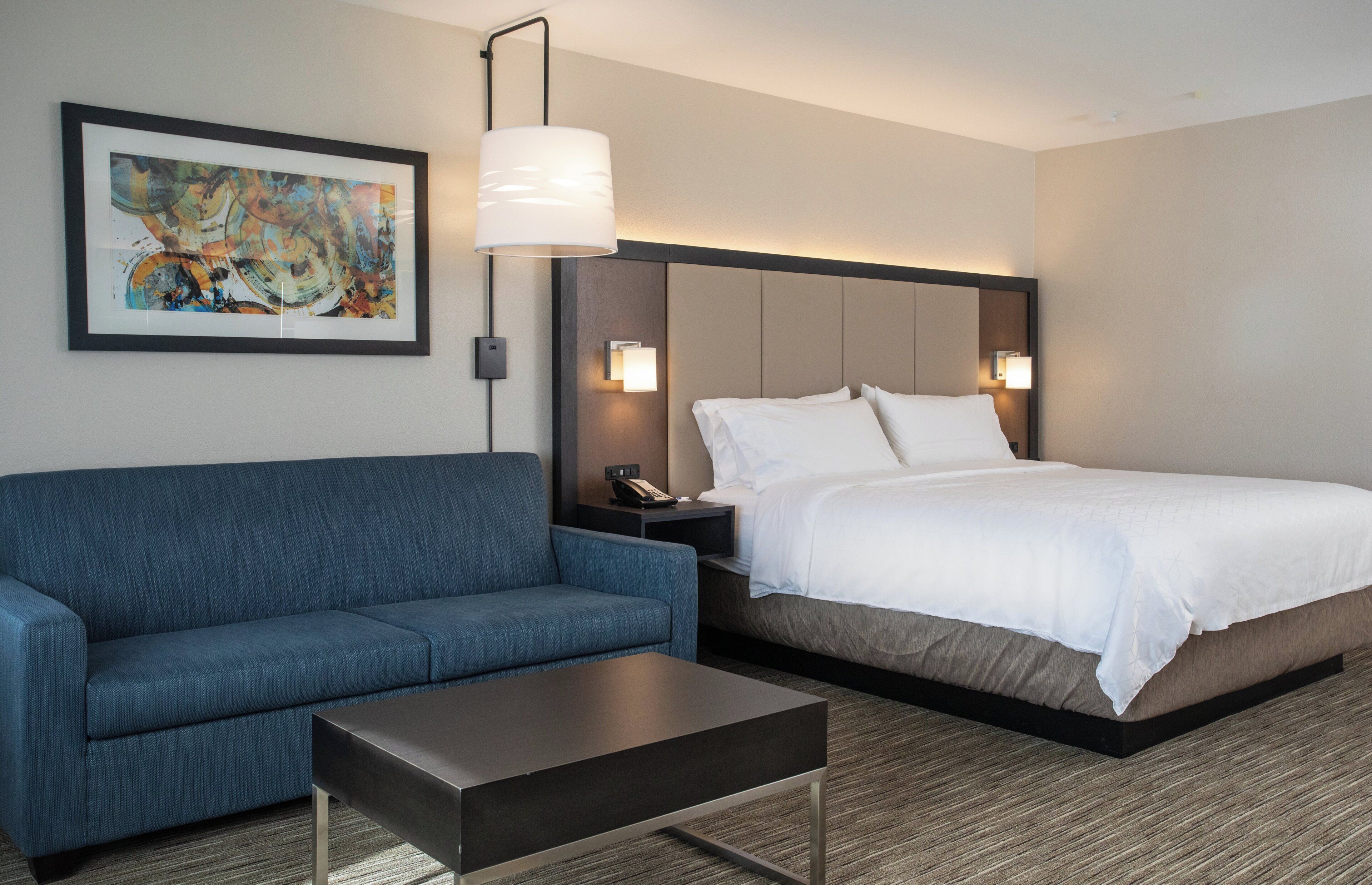 Une chambre d’hôtel avec un lit, un canapé bleu, une table basse et un tableau au mur.
