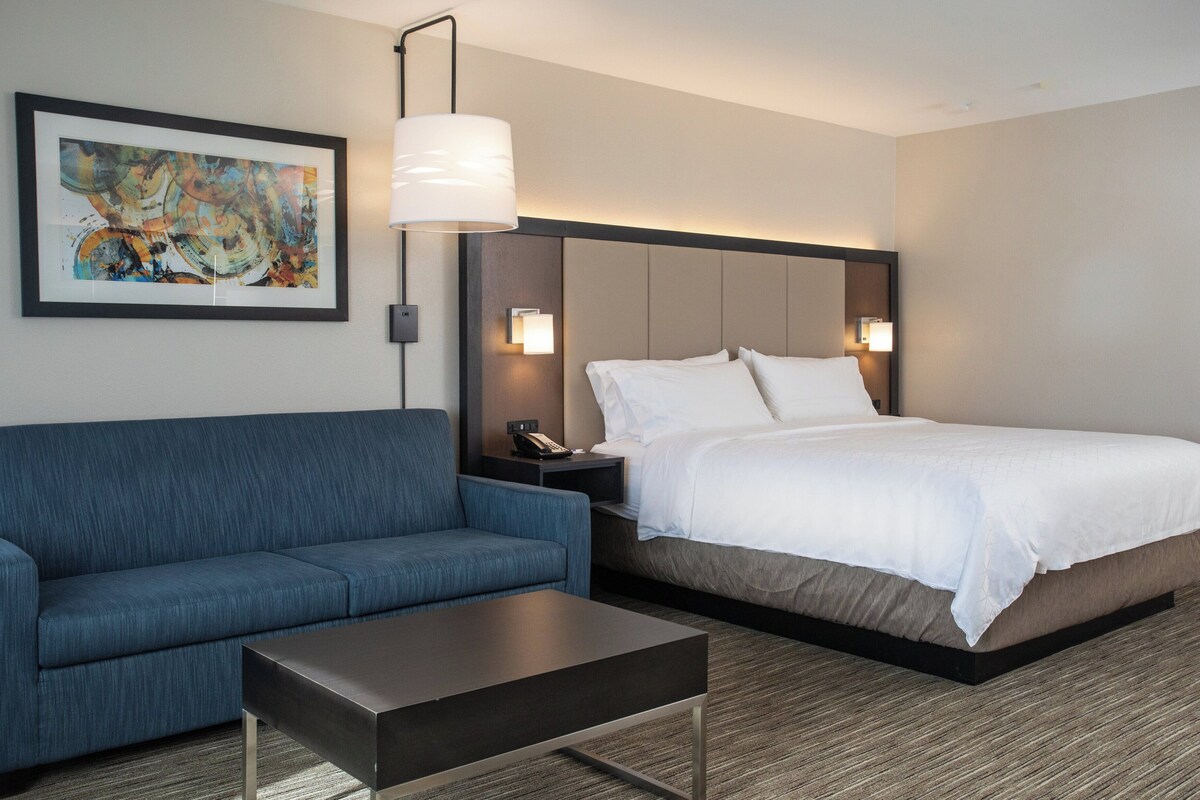 Une chambre d’hôtel avec un lit, un canapé bleu, une table basse et un tableau au mur.