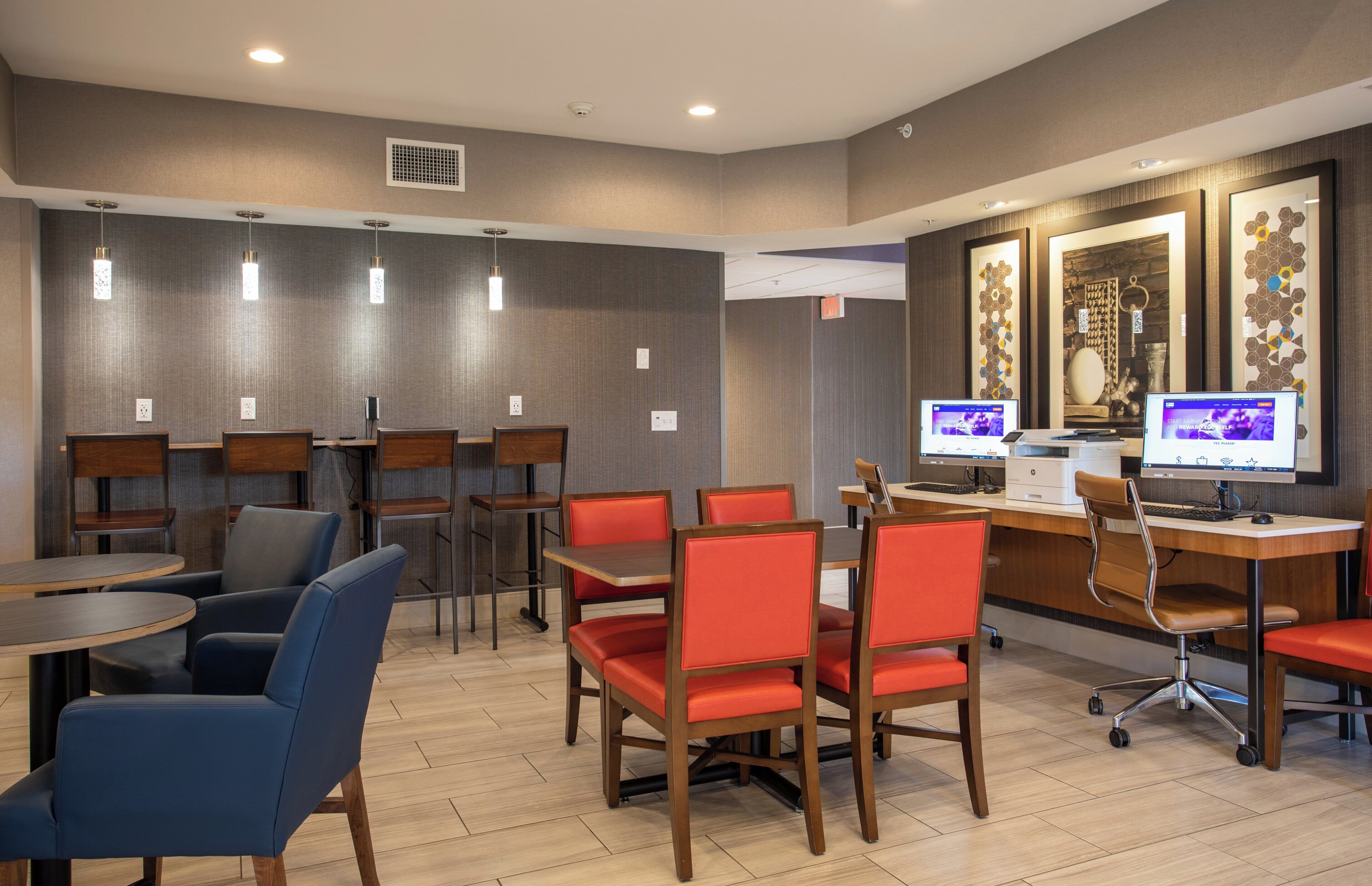 A hotel lobby with a reception desk, computers, seating area with chairs and tables, and a decorative wall.