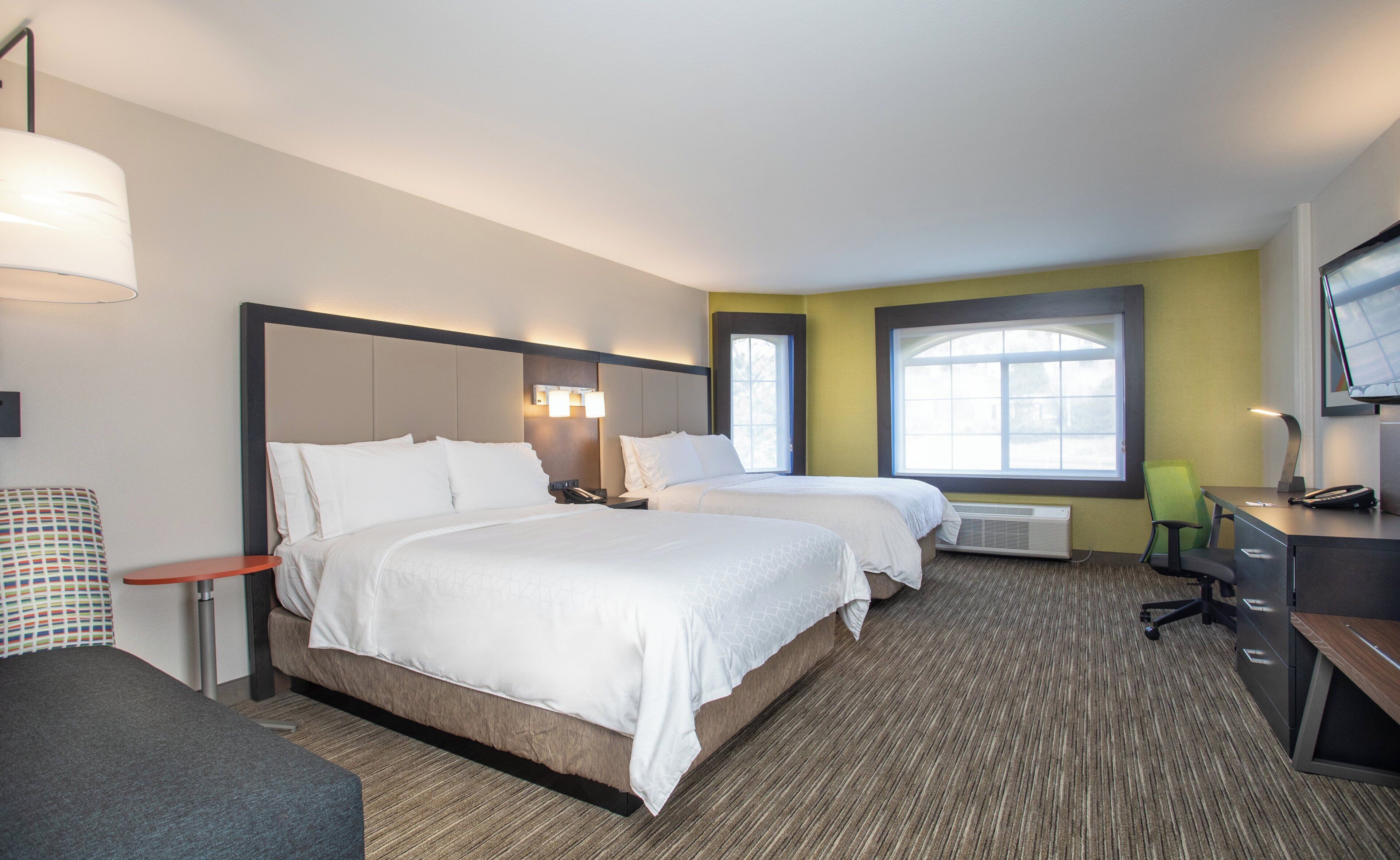 A hotel room with two beds, a desk, a chair, a TV, and a window.