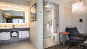 A modern bathroom with a large mirror, a glass shower enclosure, a toilet, and a chair.