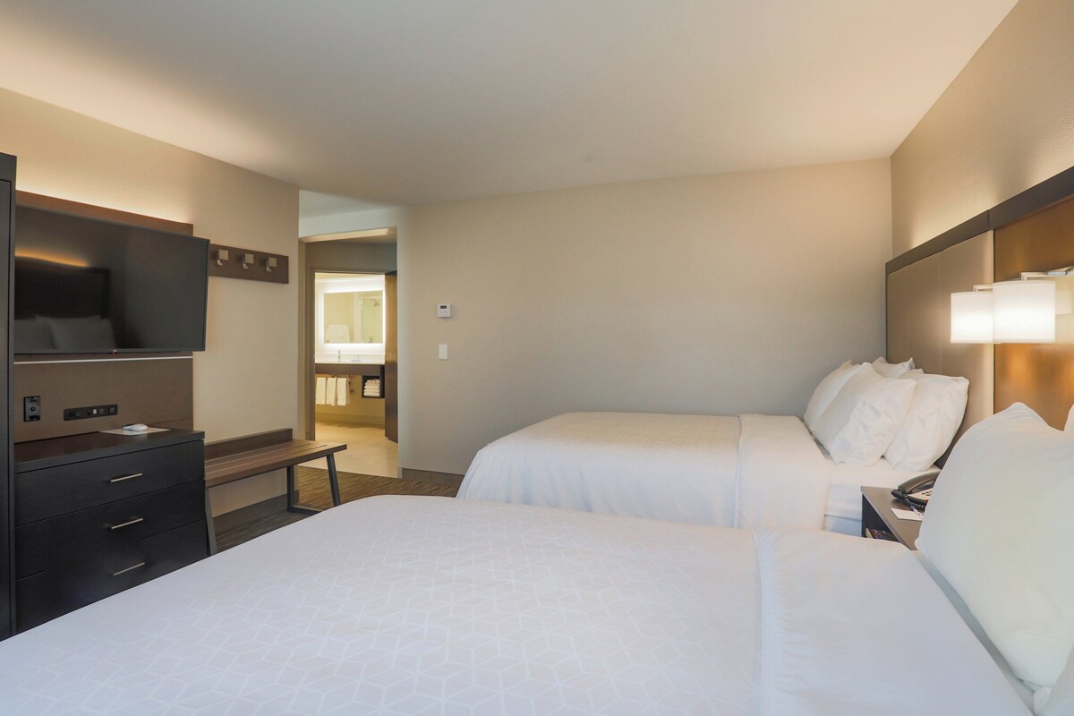 Une chambre d’hôtel avec deux lits, un bureau, une télévision et une salle de bain visible à travers une porte ouverte.