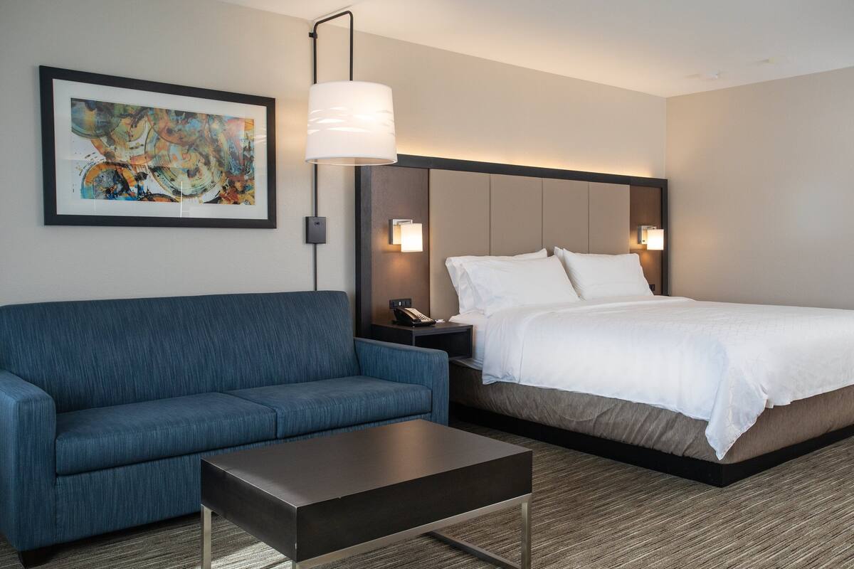 A hotel room with a bed, a blue sofa, a small table, and a painting on the wall.