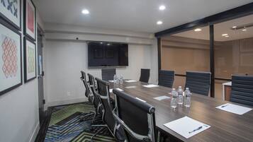 Una sala de conferencias con una larga mesa, sillas, un televisor de pantalla plana y una alfombra estampada.