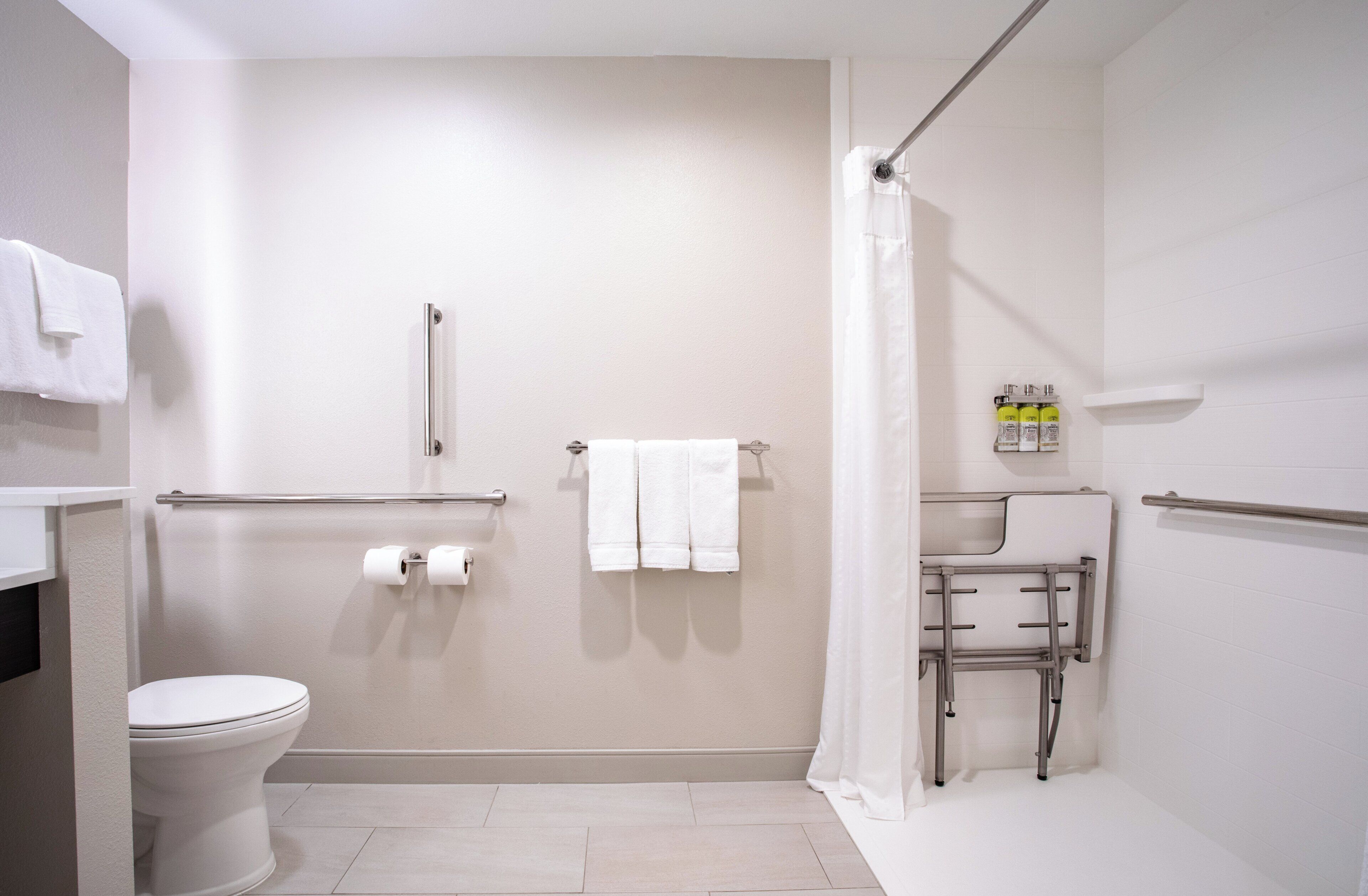 A bathroom with a toilet, a shower with a grab bar, a sink with a mirror, and a towel rack.