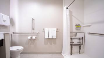 A bathroom with a toilet, a shower with a grab bar, a sink with a mirror, and a towel rack.